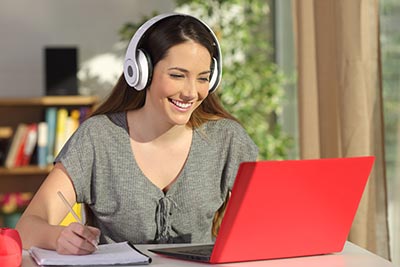 portrait of a student learning on line watching video tutorials with a red laptop and headphones in a table at home