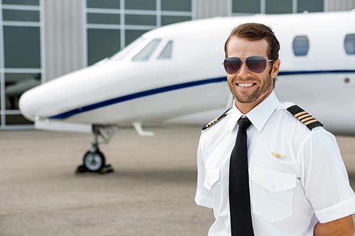 Portrait of smiling pilot with arms crossed standing in front of private jet
